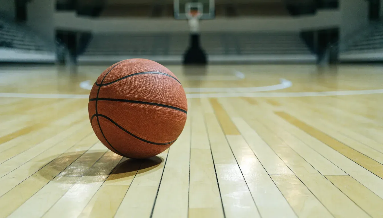 Ein Basketball liegt auf dem Parkett einer leeren Halle, von den Deckenlampen fällt gleichmässiges Licht auf den Boden.