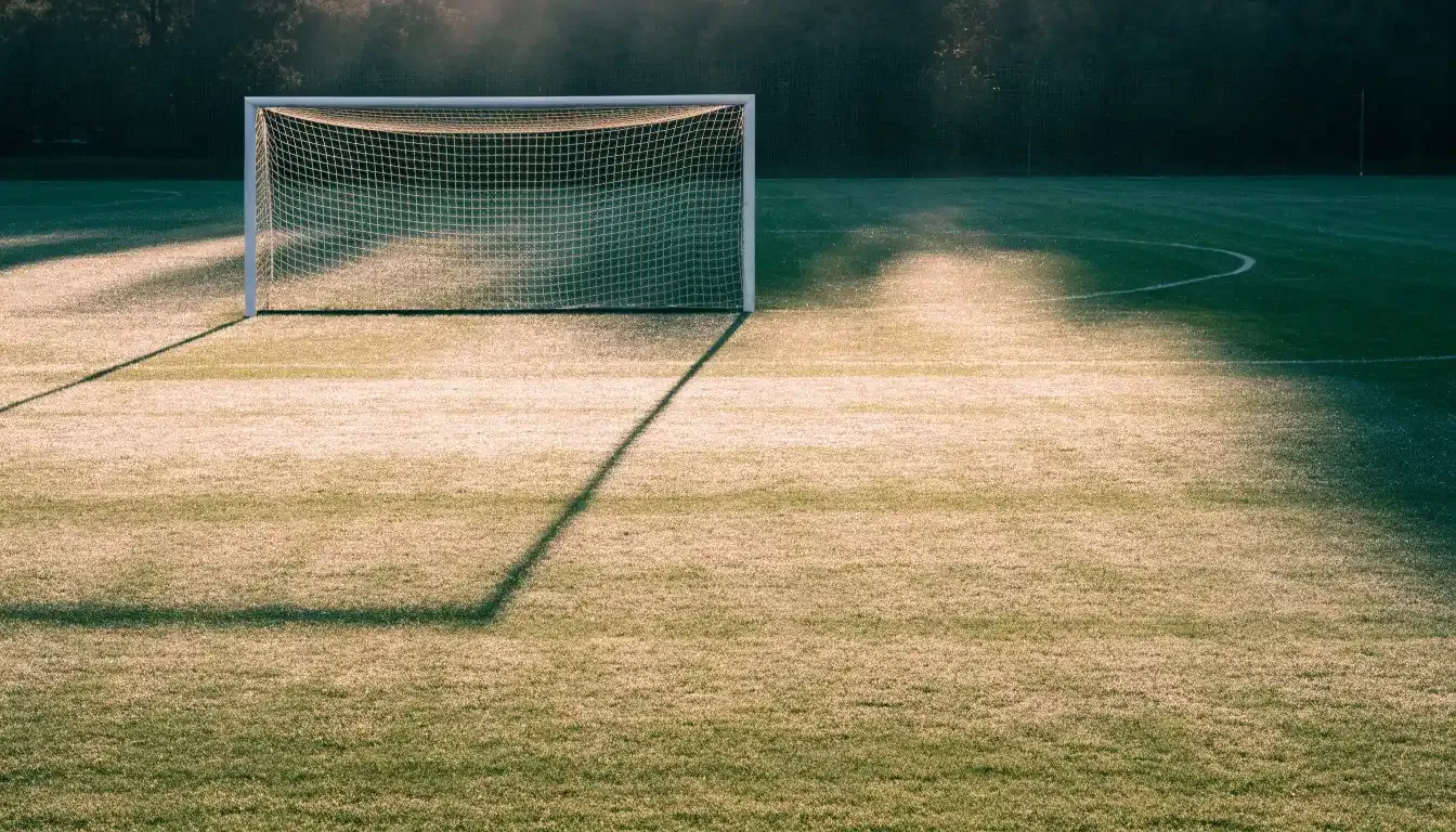 Ein Fussballtor mit Netz in der Totalen auf einem leeren Platz, Tau glänzt im Gras und die Morgensonne steht tief.